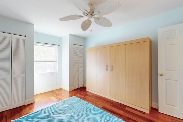 unfurnished bedroom featuring multiple closets, ceiling fan, and wood-type flooring