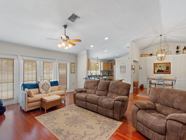 living room featuring wood finished floors, visible vents, lofted ceiling, crown molding, and ceiling fan with notable chandelier