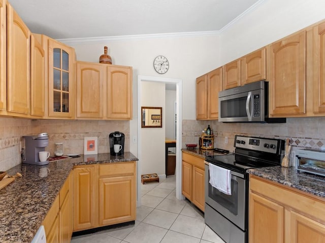 kitchen featuring ornamental molding, dark stone countertops, stainless steel appliances, light tile patterned flooring, and glass insert cabinets