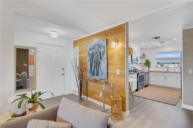 interior space with wooden walls, white cabinets, stainless steel appliances, and light wood-type flooring