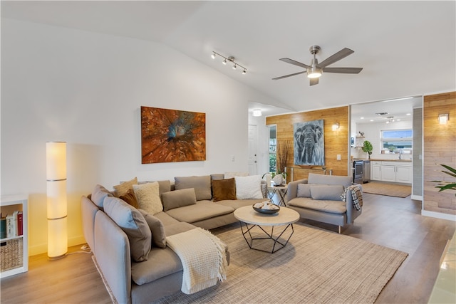 living room with ceiling fan, wooden walls, lofted ceiling, and light wood-type flooring