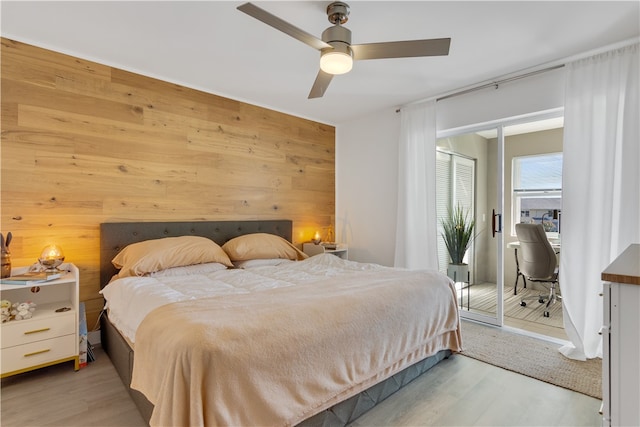 bedroom with ceiling fan, wooden walls, and light hardwood / wood-style flooring