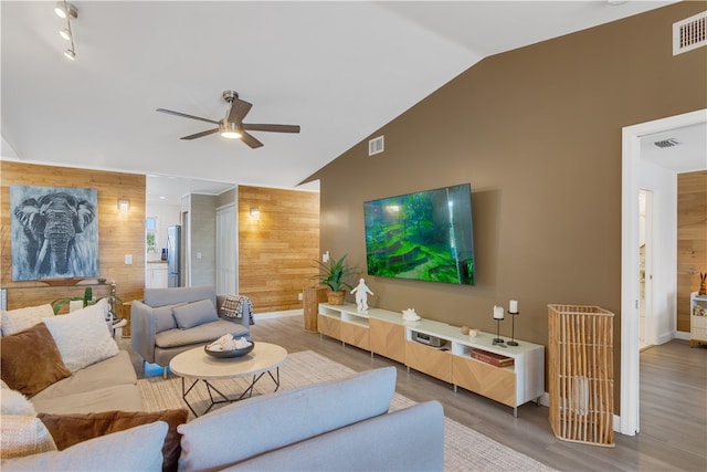 living room with hardwood / wood-style flooring, ceiling fan, lofted ceiling, and wooden walls