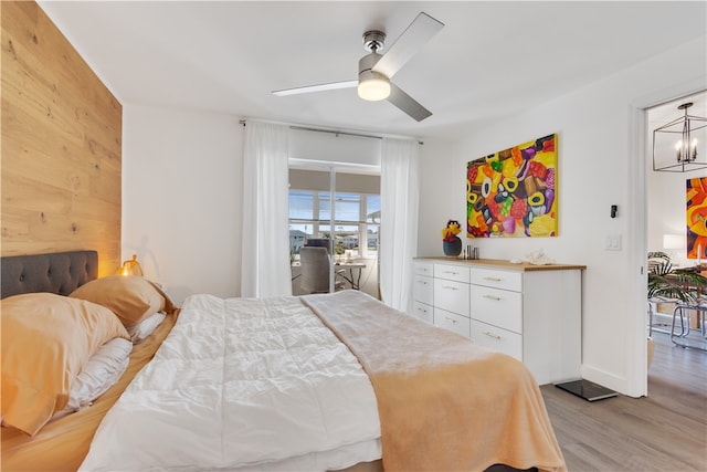 bedroom with ceiling fan with notable chandelier, light wood-type flooring, and wooden walls