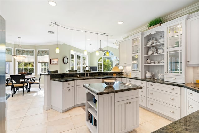 kitchen featuring a center island with sink, sink, white cabinetry, dark stone counters, and hanging light fixtures