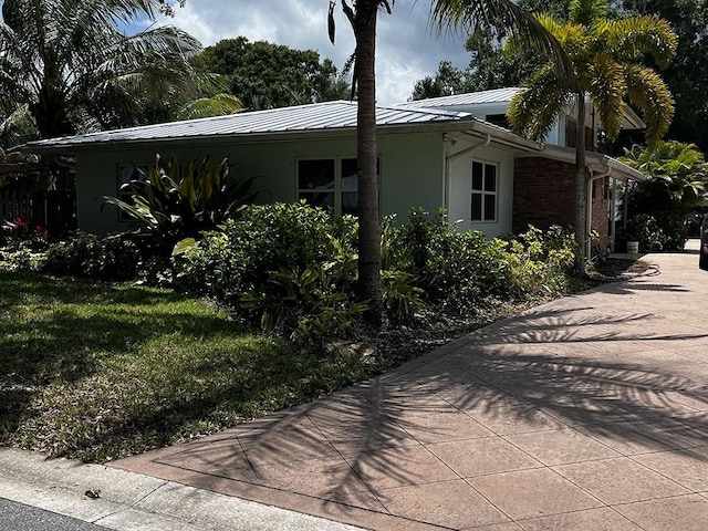 1555 33rd Ave, Vero Beach, FL 32960 - view of side of home featuring stucco siding, metal roof, concrete driveway, a standing seam roof, and a lawn