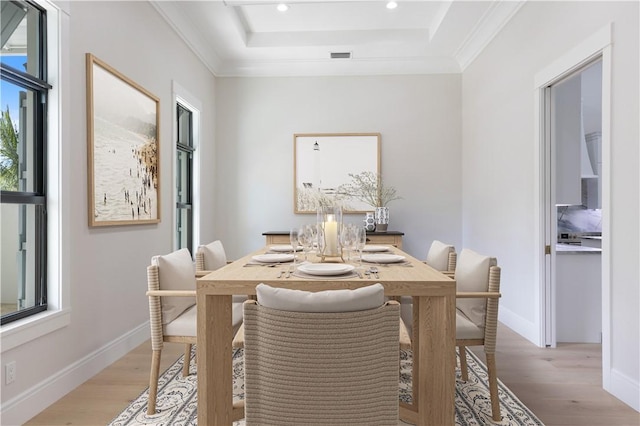 dining area with a tray ceiling, crown molding, and light hardwood / wood-style floors