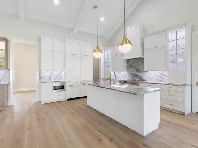 kitchen featuring white cabinets, a center island with sink, decorative backsplash, and beam ceiling