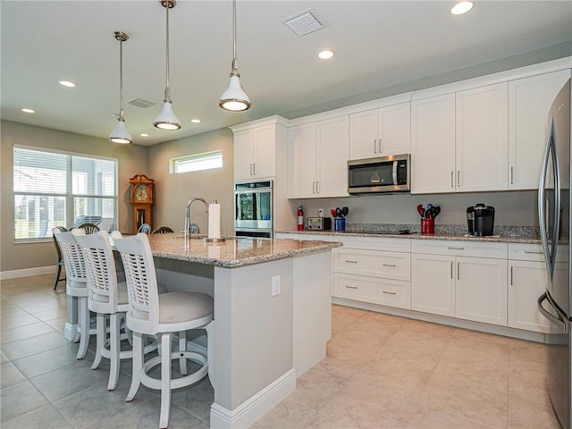 kitchen featuring a kitchen island with sink, sink, hanging light fixtures, appliances with stainless steel finishes, and white cabinetry