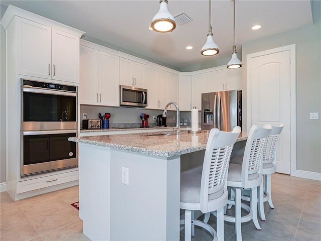 kitchen featuring light stone countertops, white cabinetry, stainless steel appliances, and a kitchen island with sink