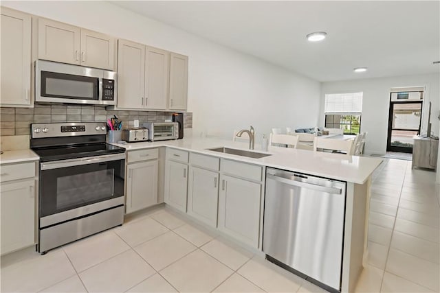 kitchen with stainless steel appliances, tasteful backsplash, light countertops, a sink, and a peninsula