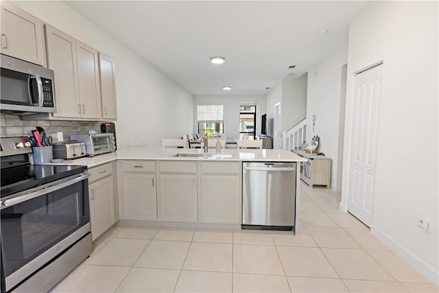 kitchen featuring light countertops, appliances with stainless steel finishes, light tile patterned flooring, a sink, and a peninsula