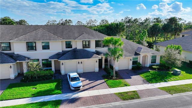 view of front of house featuring an attached garage, roof with shingles, decorative driveway, stucco siding, and a front lawn