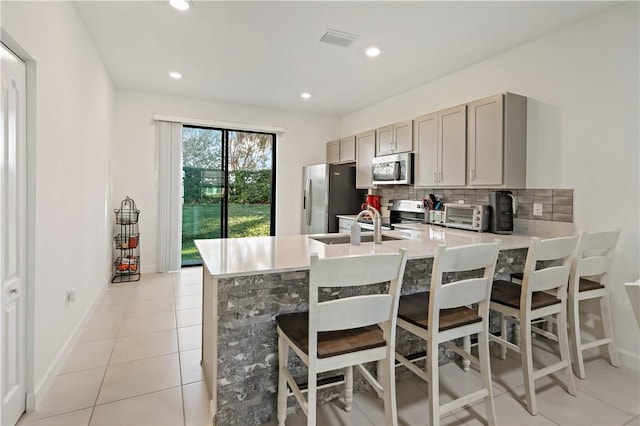 kitchen featuring light tile patterned floors, appliances with stainless steel finishes, a peninsula, light countertops, and backsplash