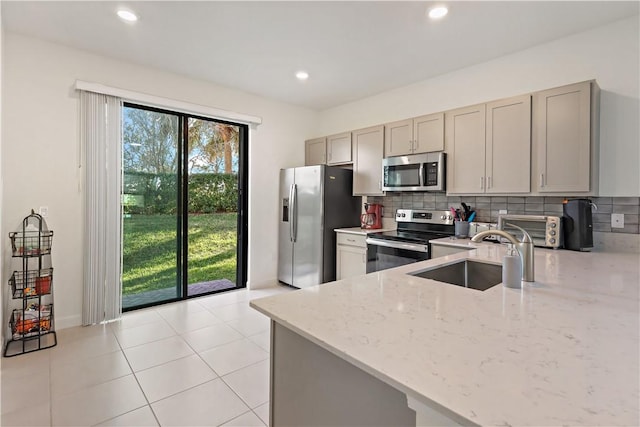 kitchen featuring a toaster, stainless steel appliances, decorative backsplash, gray cabinetry, and a sink