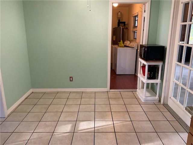 spare room featuring light tile patterned floors, water heater, baseboards, and washer and dryer