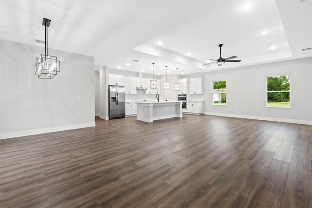 unfurnished living room with dark hardwood / wood-style flooring, a raised ceiling, ceiling fan, and sink