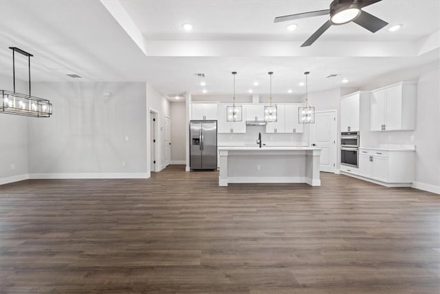 kitchen featuring appliances with stainless steel finishes, dark wood-type flooring, decorative light fixtures, a center island with sink, and white cabinetry