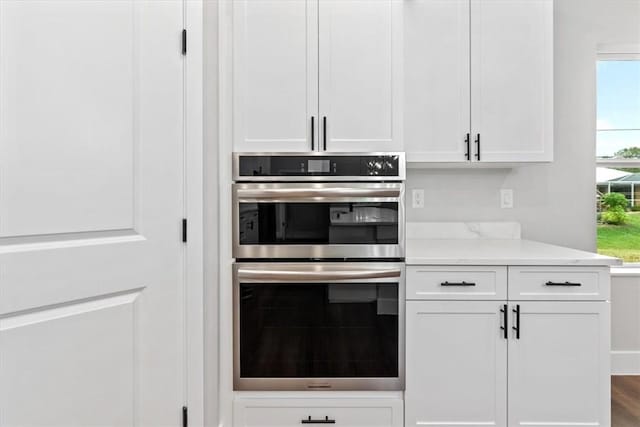 kitchen featuring hardwood / wood-style floors, white cabinetry, and stainless steel double oven