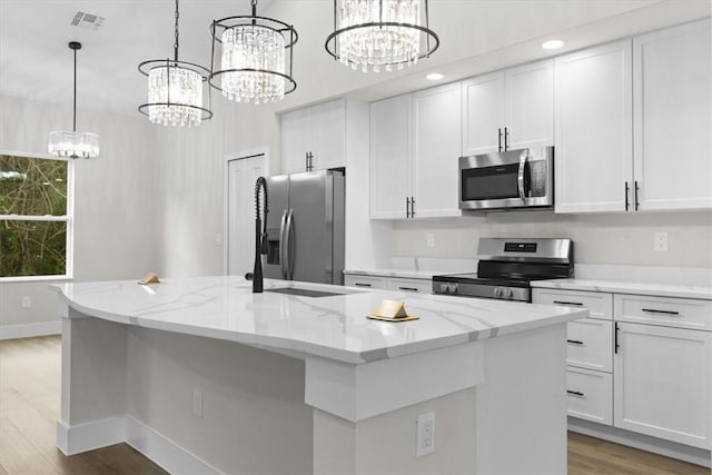 kitchen featuring white cabinetry, appliances with stainless steel finishes, hanging light fixtures, and an island with sink