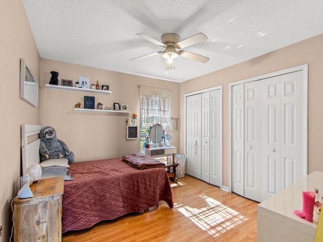 bedroom featuring light wood-style flooring, two closets, a ceiling fan, and a textured ceiling