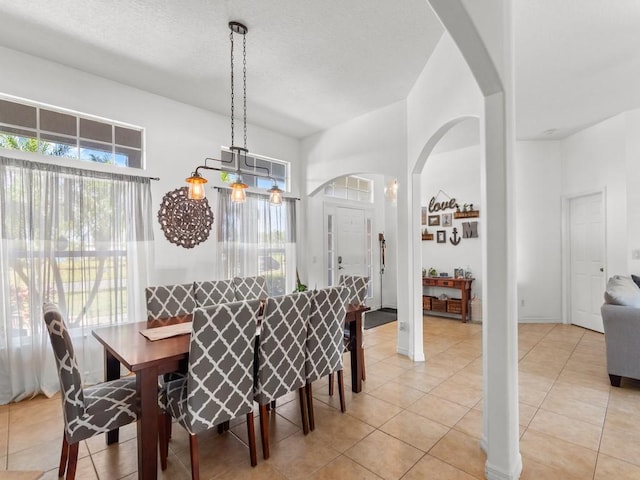 dining room featuring a wealth of natural light, arched walkways, a textured ceiling, and light tile patterned floors