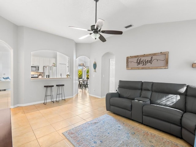 living area featuring visible vents, a ceiling fan, arched walkways, light tile patterned flooring, and vaulted ceiling