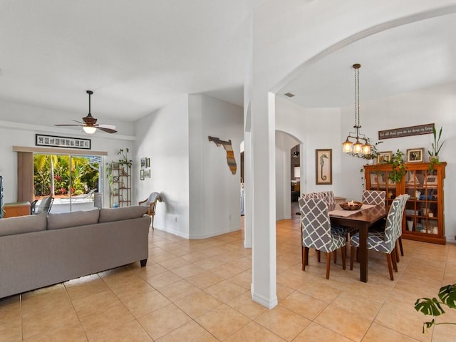 dining space with arched walkways, light tile patterned floors, ceiling fan with notable chandelier, and baseboards