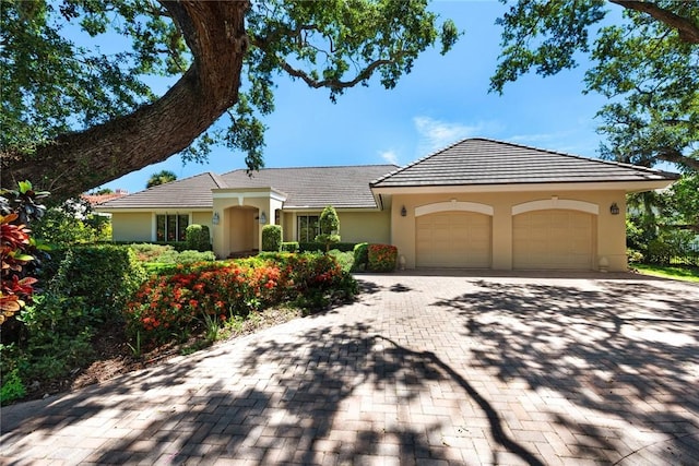 ranch-style home featuring decorative driveway, a tile roof, an attached garage, and stucco siding