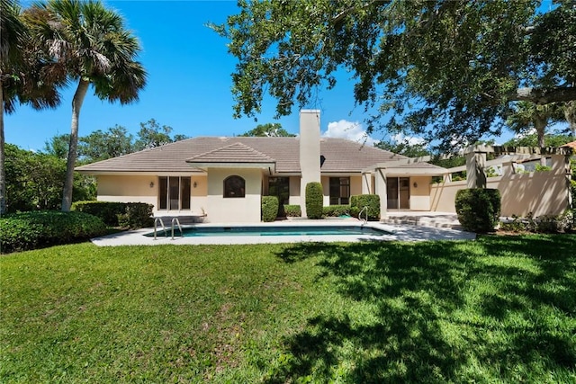 back of house featuring an outdoor pool, a chimney, a tiled roof, a yard, and stucco siding