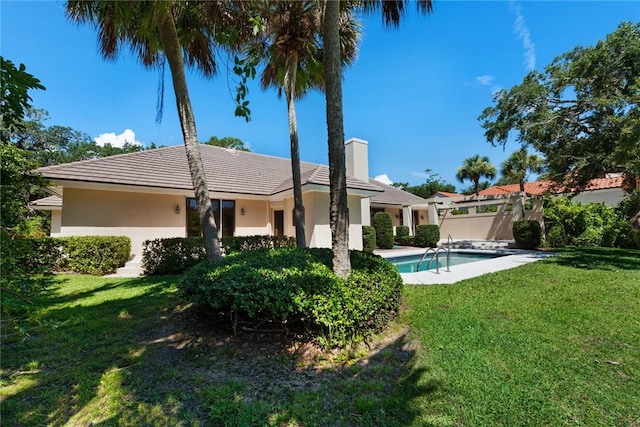 rear view of property with an outdoor pool, a tiled roof, a lawn, stucco siding, and a chimney