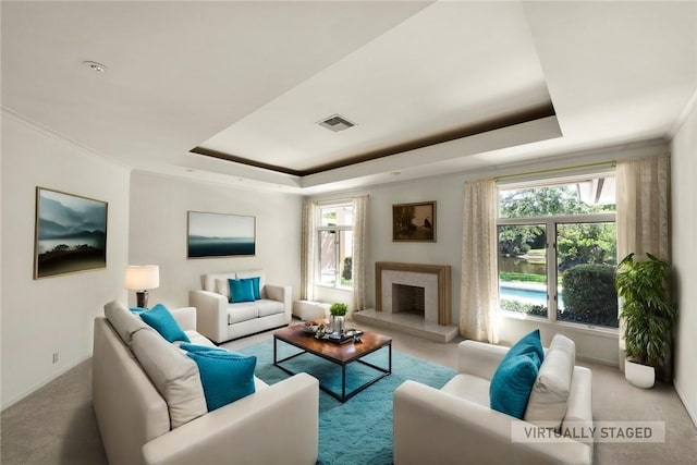 carpeted living room with a tray ceiling, a premium fireplace, visible vents, and crown molding