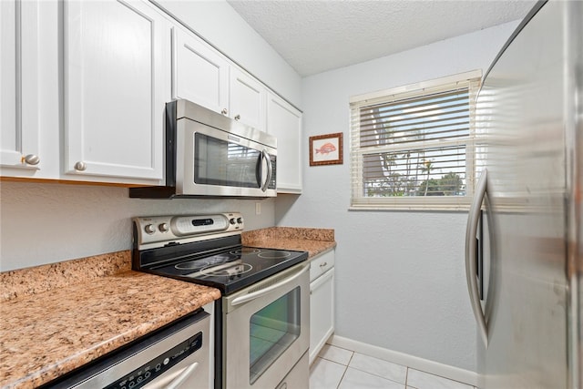 kitchen featuring white cabinetry, light stone counters, appliances with stainless steel finishes, a textured ceiling, and light tile patterned floors