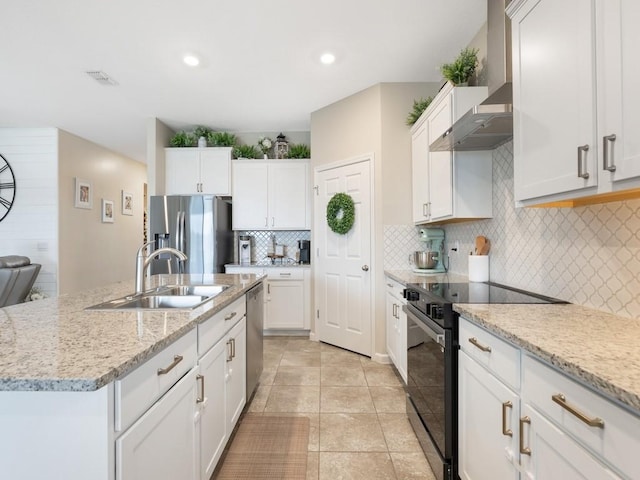 kitchen with appliances with stainless steel finishes, a center island with sink, white cabinetry, and wall chimney range hood