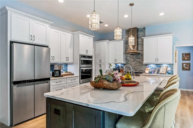 kitchen featuring stainless steel appliances, wall chimney range hood, a spacious island, decorative light fixtures, and white cabinets