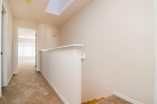 corridor with lofted ceiling with skylight, an upstairs landing, baseboards, and carpet floors