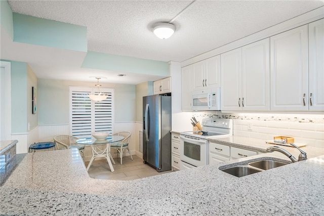 kitchen with a textured ceiling, decorative light fixtures, sink, white cabinets, and white appliances