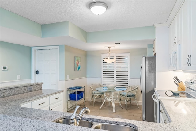 kitchen with a textured ceiling, pendant lighting, sink, white cabinets, and white appliances