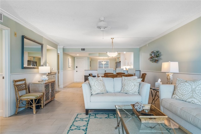 living room featuring a textured ceiling, light hardwood / wood-style floors, ornamental molding, and ceiling fan