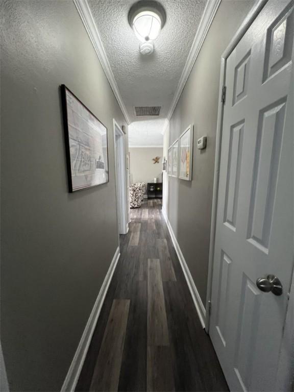 hallway featuring a textured ceiling, crown molding, dark wood-style flooring, and baseboards