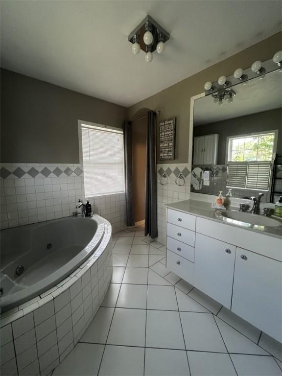 bathroom featuring tile walls, a whirlpool tub, tile patterned floors, vanity, and wainscoting