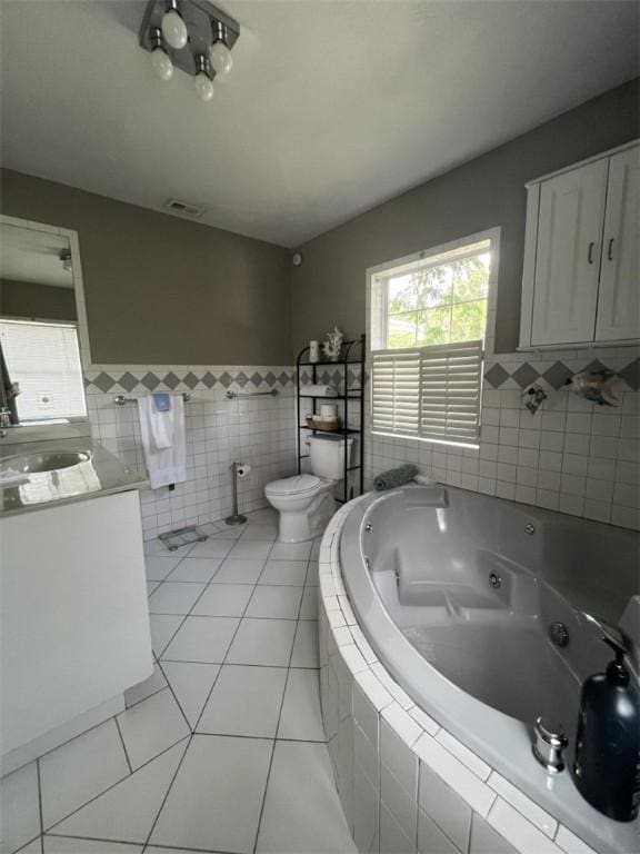 bathroom with tile walls, tile patterned flooring, toilet, a tub with jets, and vanity