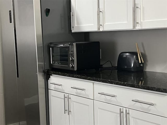 kitchen with white cabinetry, dark stone counters, and freestanding refrigerator