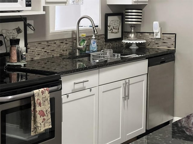 kitchen featuring stainless steel appliances, backsplash, white cabinets, dark stone countertops, and a sink