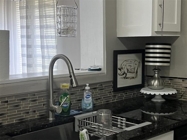 kitchen view of decorative backsplash, white cabinetry, and dark stone counters