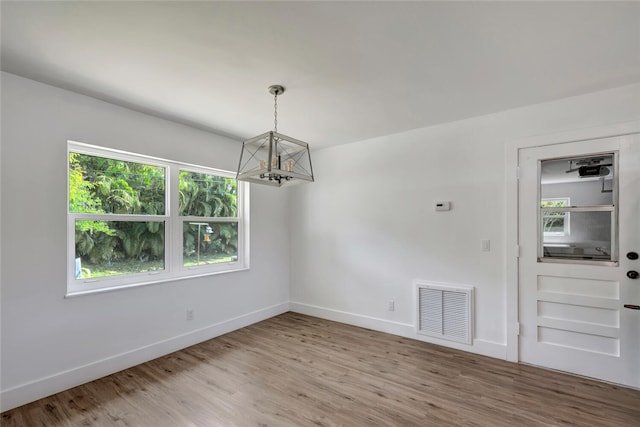 unfurnished dining area featuring a notable chandelier, wood finished floors, visible vents, and baseboards