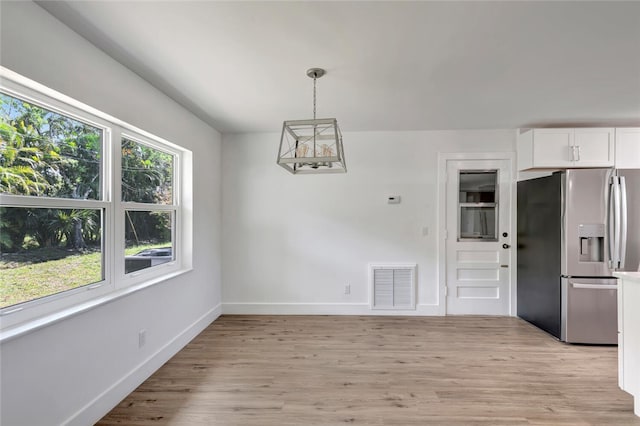 unfurnished dining area featuring light wood-type flooring, visible vents, and baseboards