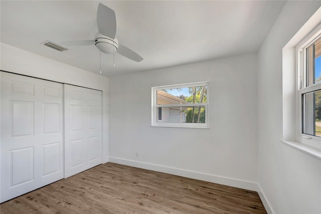 unfurnished bedroom with multiple windows, wood finished floors, visible vents, and baseboards