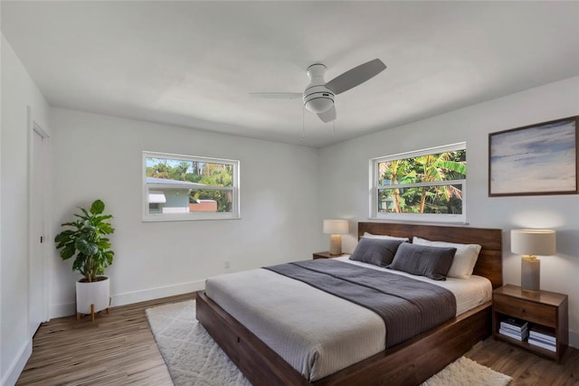 bedroom with multiple windows, wood finished floors, a ceiling fan, and baseboards