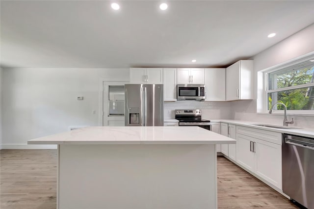 kitchen featuring light wood finished floors, decorative backsplash, appliances with stainless steel finishes, a sink, and a kitchen island